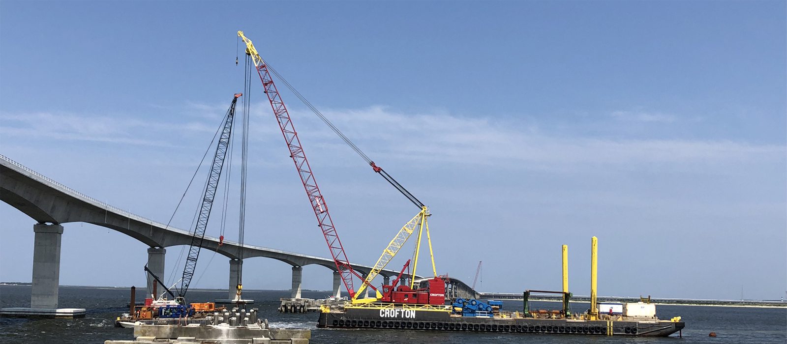 A crane is in the foreground with a bridge and water behind it.